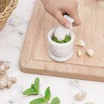 Hand grinding fresh green herbs into a paste with a white marble mortar and pestle, beside garlic, ginger and mint