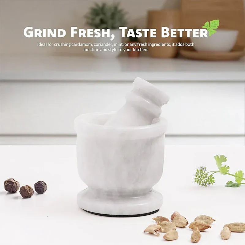 White marble mortar and pestle on a kitchen counter with whole peppercorns, cardamom pods and fresh coriander
