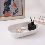 White oval marble tray holding tealights and a reed diffuser beside books