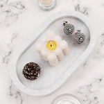 White marble oval tray holding a candle, earrings and a pinecone on marble
