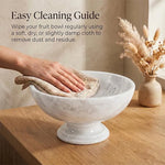 White marble pedestal fruit bowl being wiped clean with a cloth on a countertop