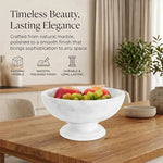 White marble pedestal fruit bowl holding fruit on a dining table, noting its natural stone and polished finish
