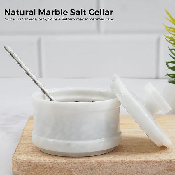 White marble stone salt keeper with spoon inside and lid leaning against it on a wooden board