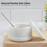 White marble stone salt keeper with spoon inside and lid leaning against it on a wooden board