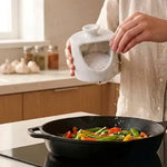 White marble salt pig held in hand pouring salt into a pan of vegetables on the stove