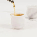 Drink being poured into a white marble shot glass on a marble surface