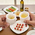 Two hands toasting with white marble shot glasses over a table of appetizers