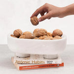 White marble trinket bowl on books, filled with walnuts, hand reaching in