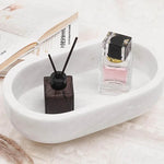 White oval marble trinket dish holding a reed diffuser and perfume beside books
