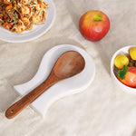 White marble utensil rest holding a wooden spoon beside a plate of noodles