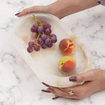 Hands holding a white onyx footed marble bowl with grapes and a peach