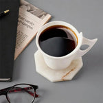White onyx octagon marble coaster under a white coffee cup beside a newspaper and glasses
