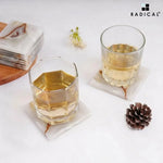 White onyx square marble coasters under two whiskey glasses on a white table