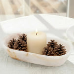 Oval white onyx marble dough bowl used as a candle centerpiece with pillar candles and pinecones