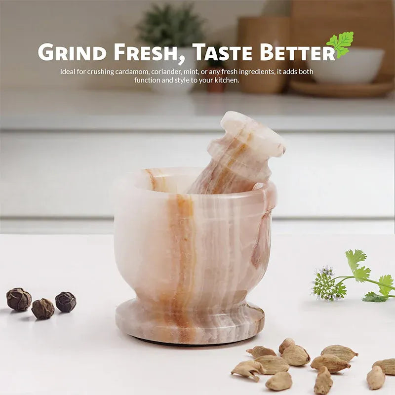 White onyx marble mortar and pestle on a kitchen counter with whole peppercorns, cardamom pods and fresh coriander