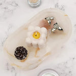 White onyx marble oval tray holding a candle, earrings and a pinecone on marble