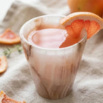 White onyx marble shot glass holding a pink grapefruit drink garnished with a citrus slice