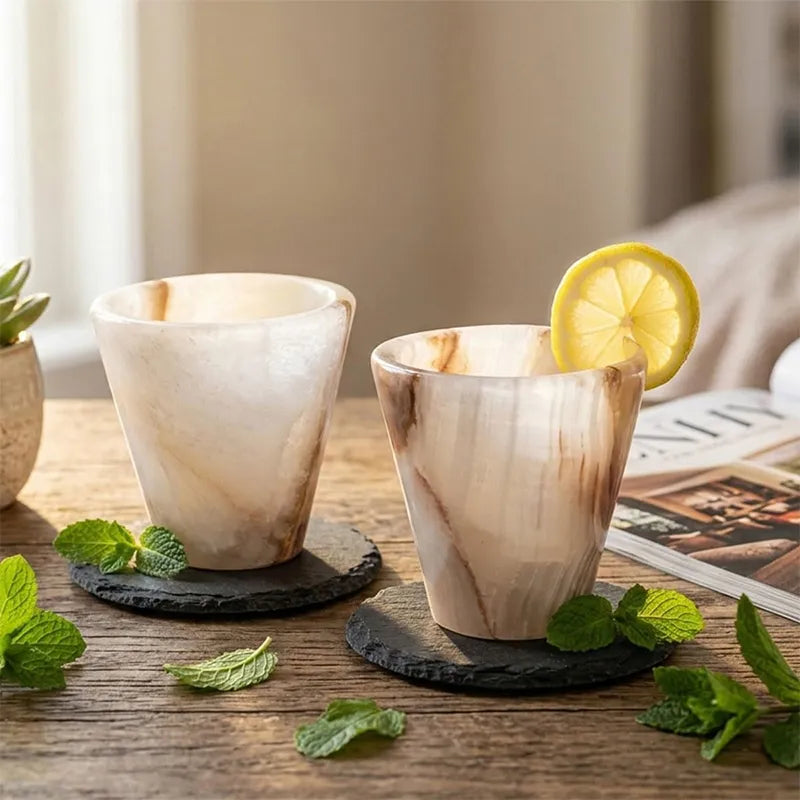 Pair of white onyx marble shot glasses garnished with lemon and mint on wood