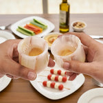 Two hands toasting with white onyx marble shot glasses over a table of appetizers