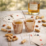 Two white onyx marble shot glasses of whiskey on a rustic table with cards and nuts