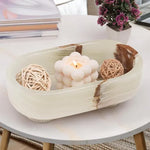 White onyx footed marble trinket bowl holding a candle and rattan balls on a coffee table