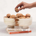 White onyx marble trinket bowl on books, filled with walnuts, hand reaching in